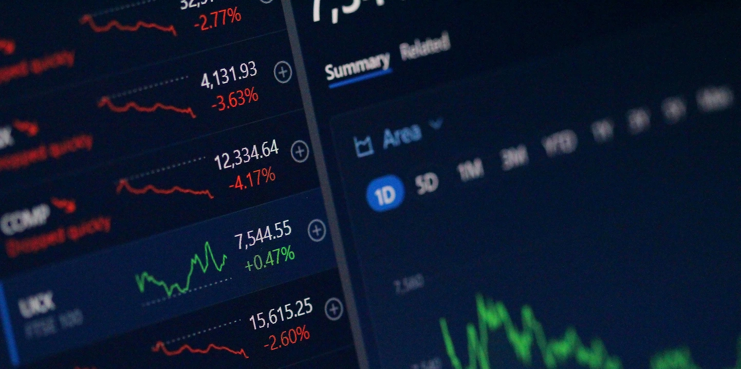 Pantalla con gráficos y cifras bursátiles que muestran variaciones de índices financieros en rojo y verde.